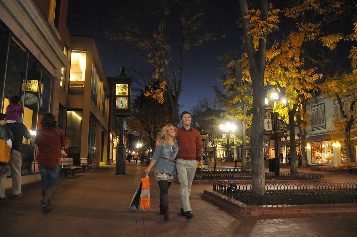 Lights illuminate the walkways of Pearl Street Mall on a fall evening where a couple with arms wrapped around each other walks with their shopping bags.