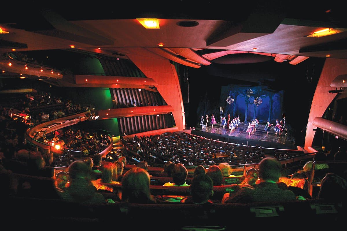 A theater is lit with red and green lights as the audience watches a visual arts performance on a stage in Denver, Colorado.