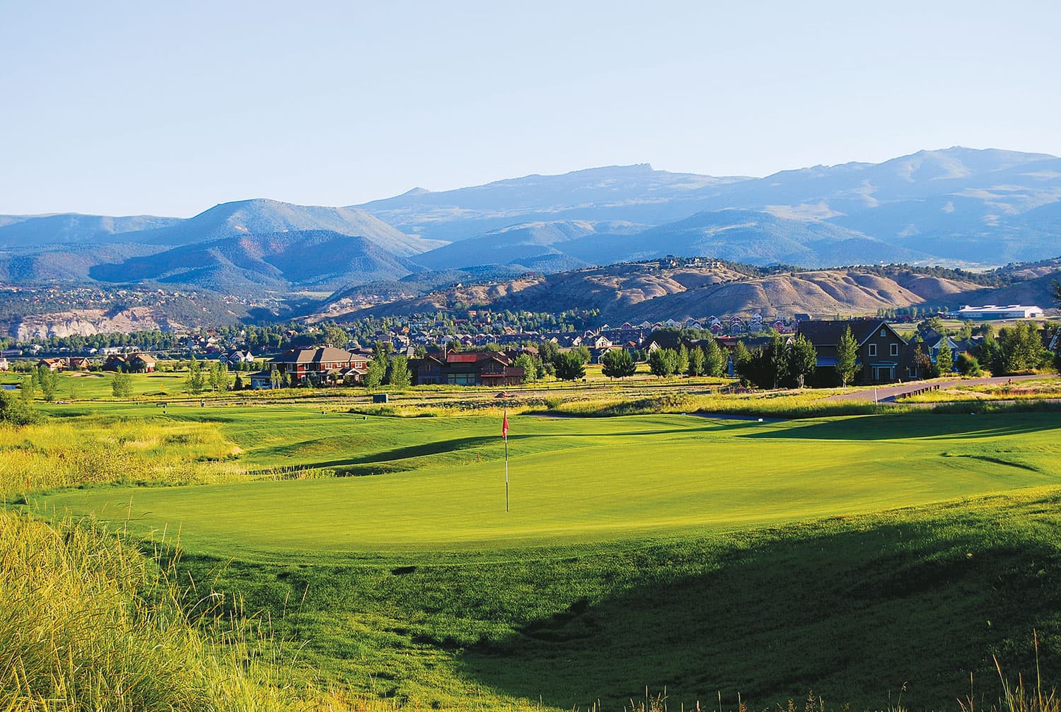 The rolling green course of Eagle Ranch Golf Course sits peacefully beneath distant, majestic, blue-and-purple mountains.