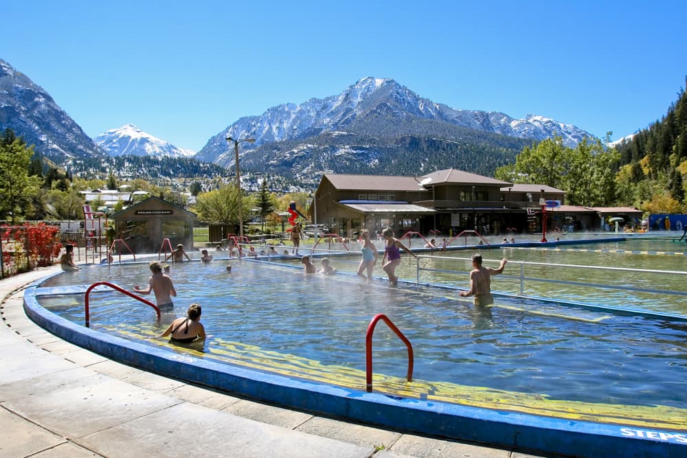 The sky is blue, a mountain peak is barely dusted with snow and a hot-springs pool filled with romping kids and adults in steaming waters