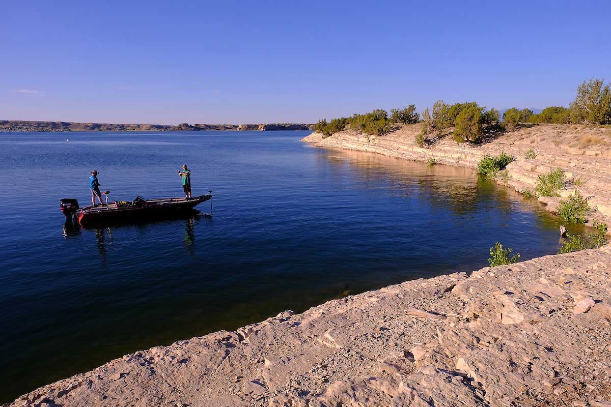 Two people stand on a small motorized fishing boat that is anchored on the water at Lake Pueblo State Park.