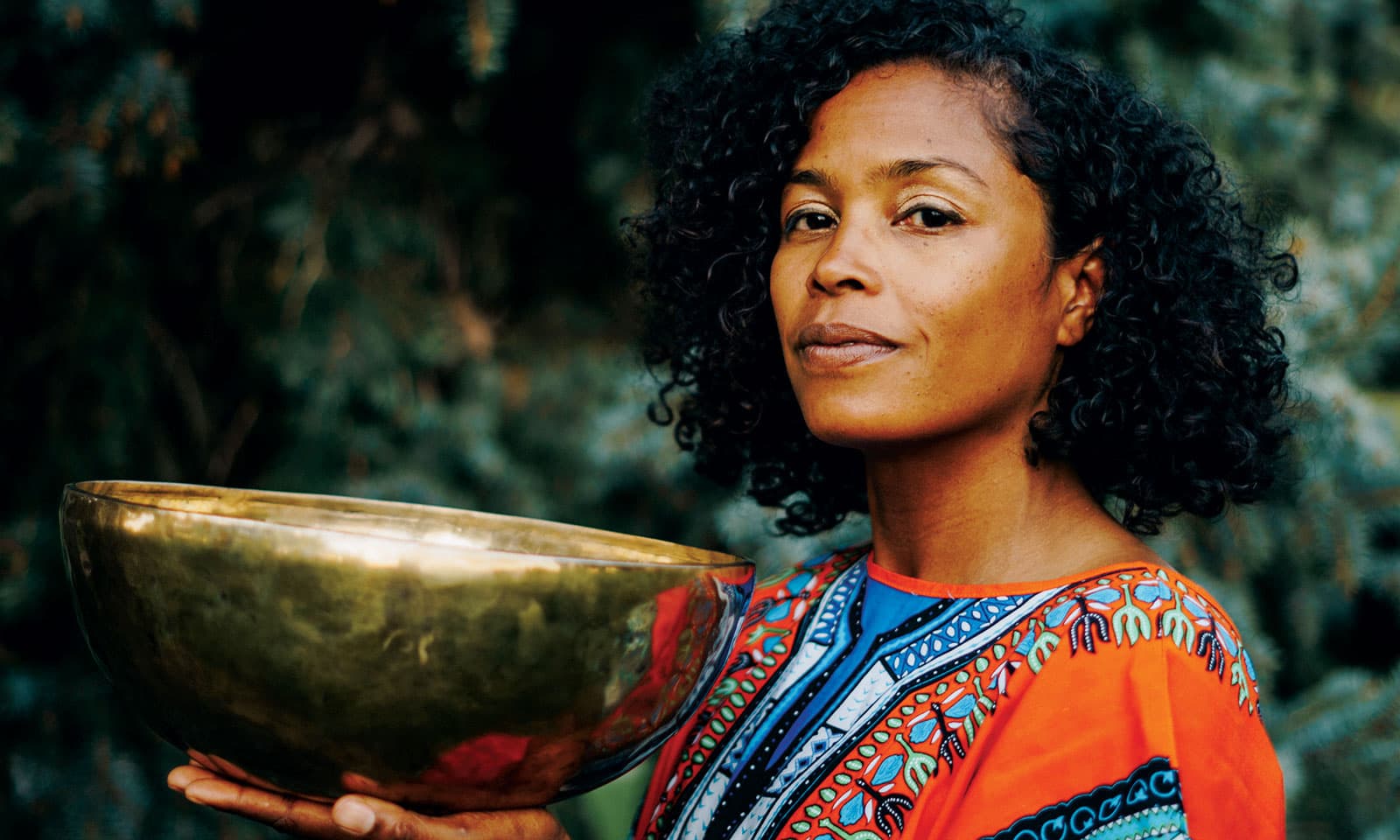 A person in a deep-orange shirt with blue stitched patterns balances a large, worn, bronze bowl in their hand in Denver, Colorado.