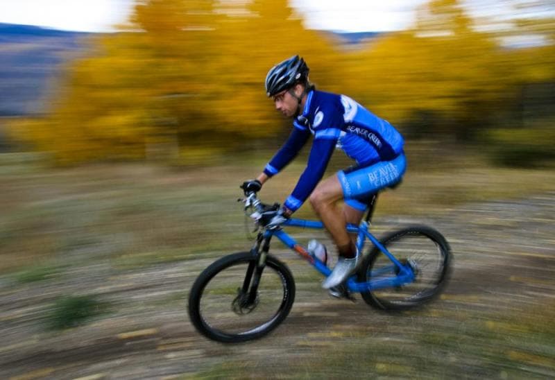 A mountain biker in bright blue, speeds past golden aspens on a rocky trail.