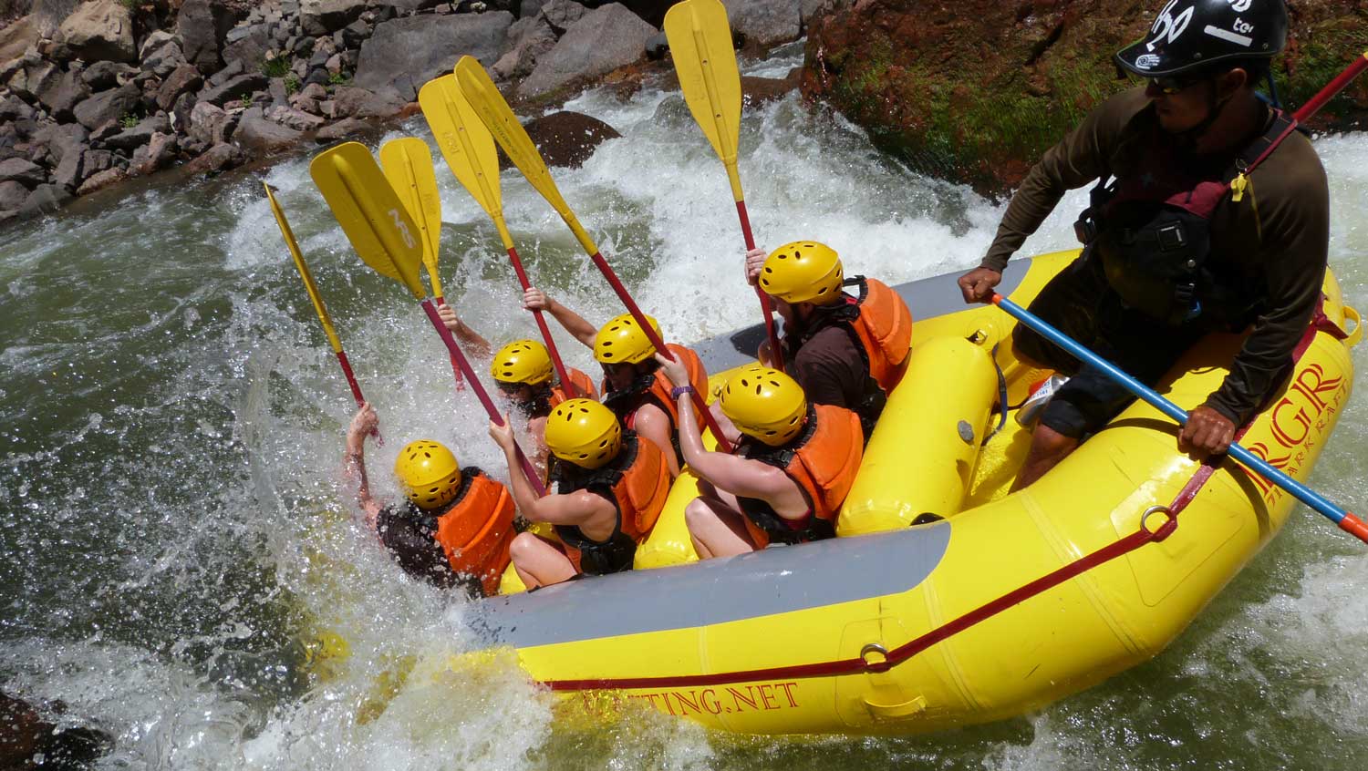 A group of people in orange life vests splash through a whitewater rapid in the Royal Gorge