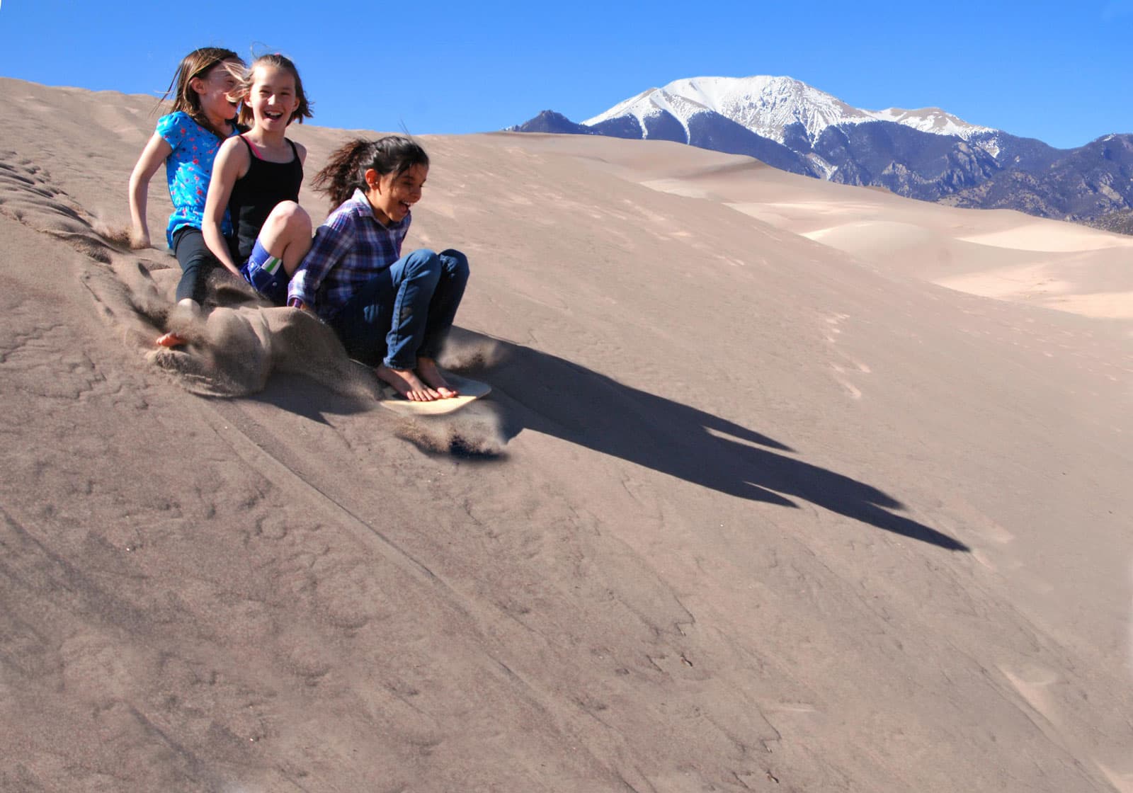 A group of laughing children having fun sledding down sand dunes