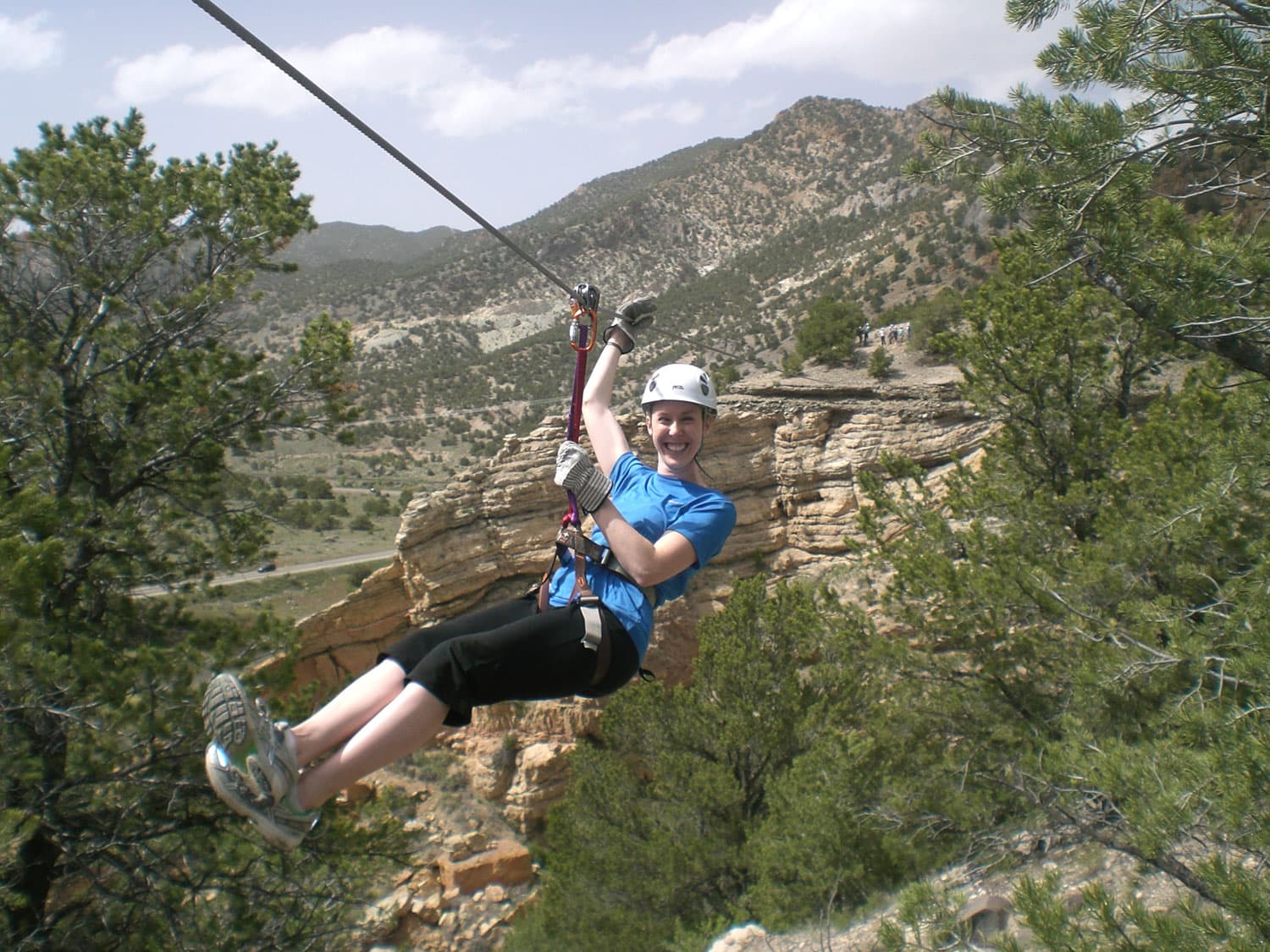 An adventurer in a blue shirt and black pants smiles and whizzes down a zipline in Salida, Colorado.