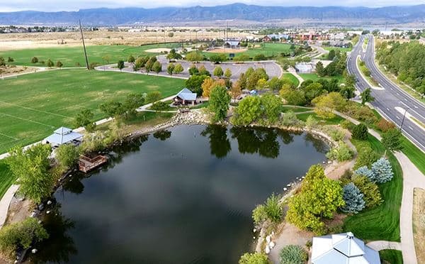 A dark lake sits in a park with picnic shelters around the shore. On the right there's a four-lane road that leads toward the Front Range mountains.