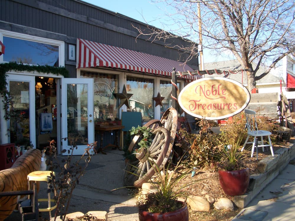 On Lafayette's Public Road, the antique shop Noble Treasures sits in the sun. The shop has a red and white striped awning and the front door is open.