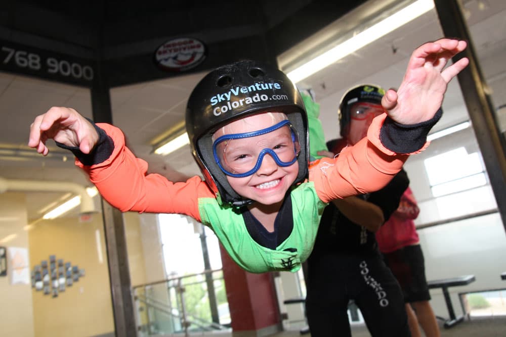 A kid in a helmet smiles as he's indoor skydiving at SkyVenture Colorado outside Denver in Lone Tree, CO