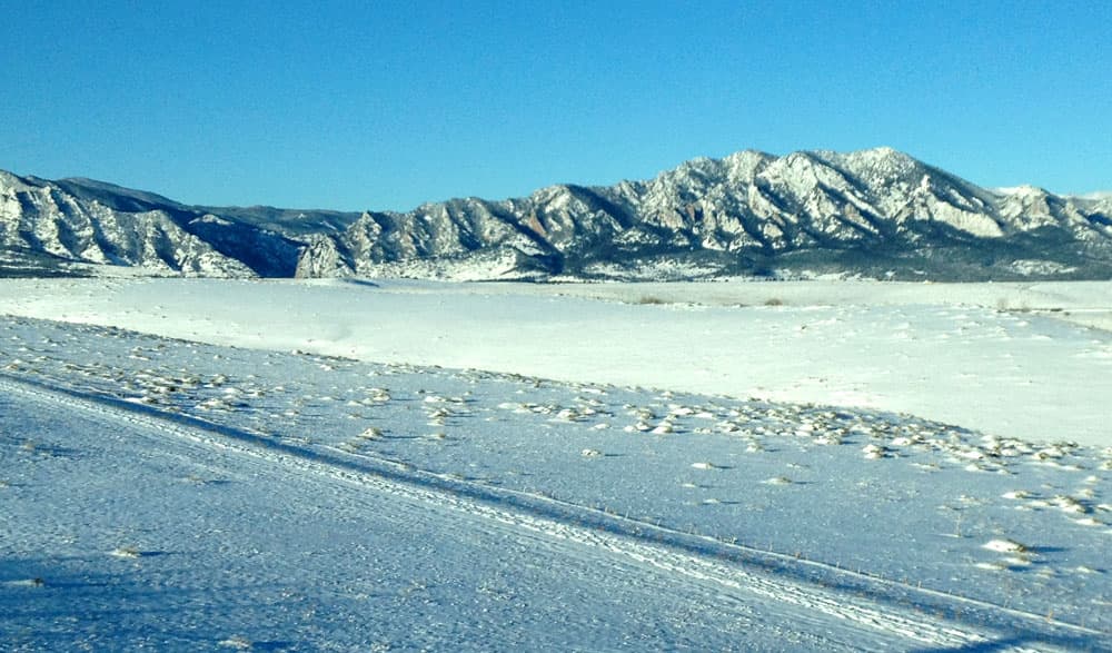 Snow covers the Flatiron mountains in the distance. In the foreground, snow covers the valley and all the land surrounding near Superior.