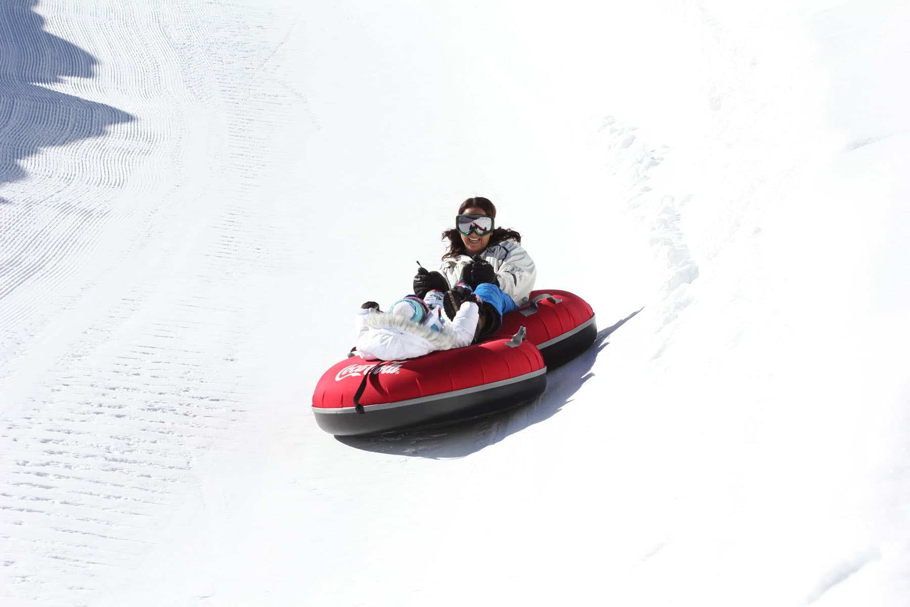 Two people in red tubes snow tube down a snowy path.