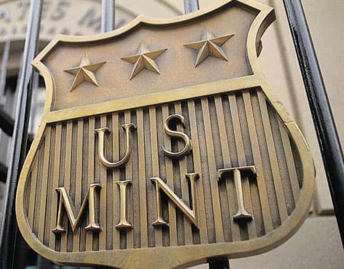 A bronze plaque reads "U.S. Mint." It has three stars on top of it and apperas to hang from a fence