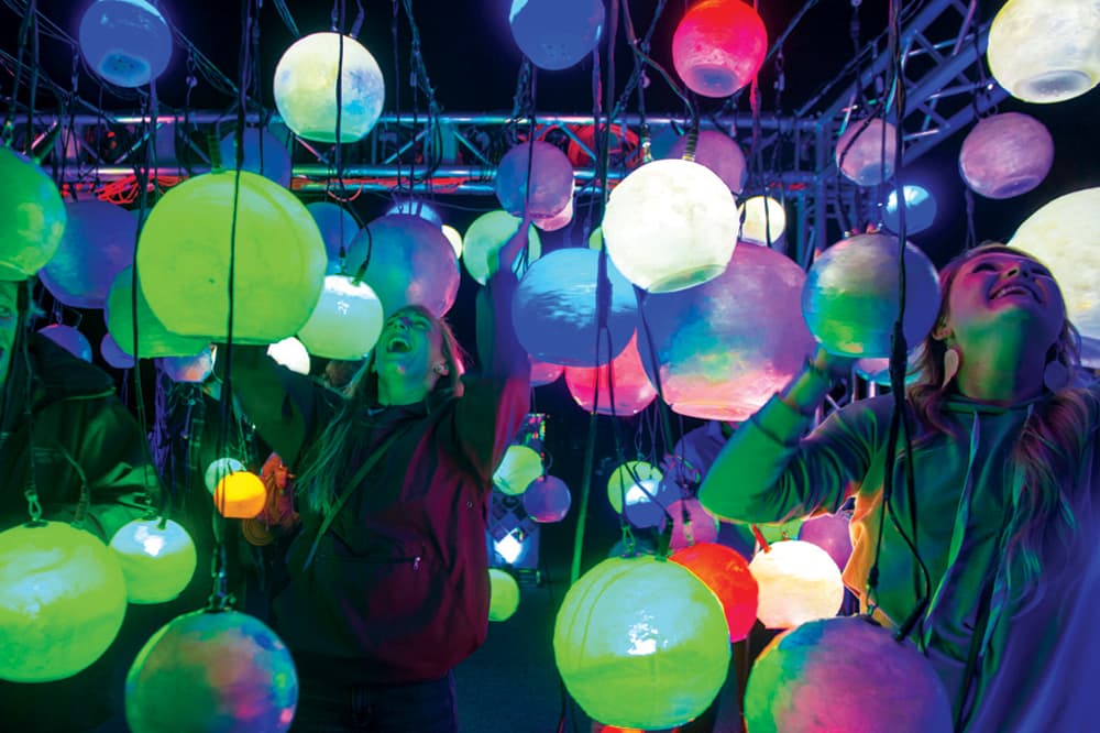 Two people smile widely amid dozens of multi-colored, glowing spheres at the Breckenridge International Festival of Arts.