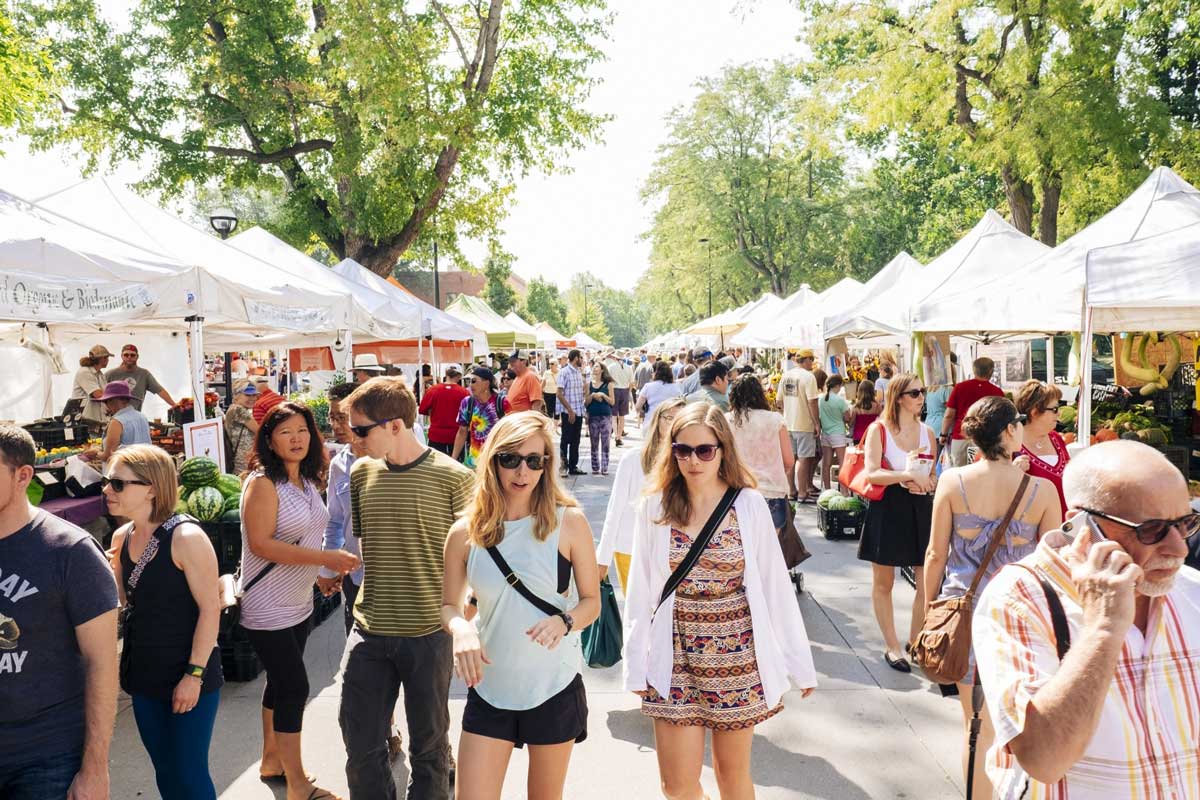 Two people walk between the crowded stalls at the farmers' market