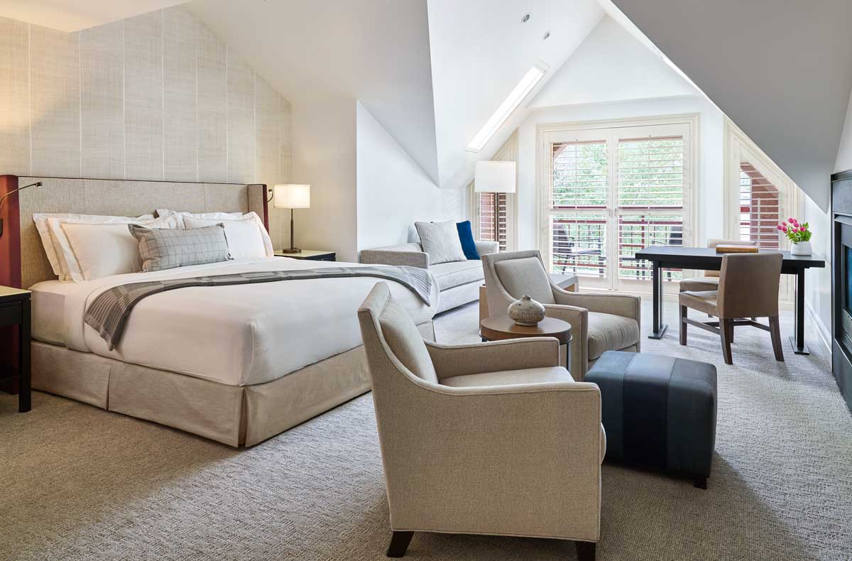 A room filled with soft fabrics and earth tones, with a king-size bed, two lounge chairs and a balcony