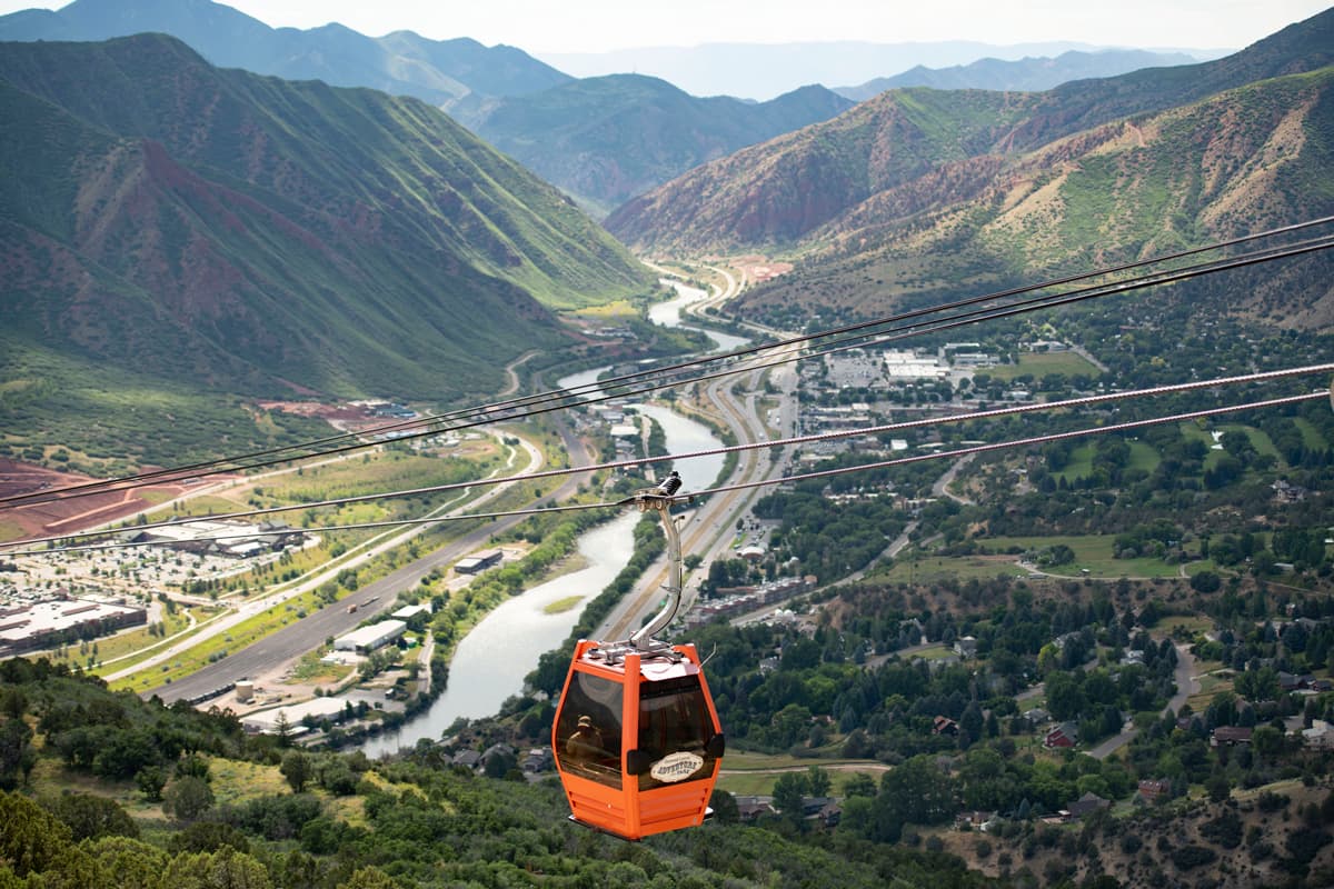 The red-orange Glenwood Gondola climbs above the Colorado River and the surrounding lush canyon walls and valley.