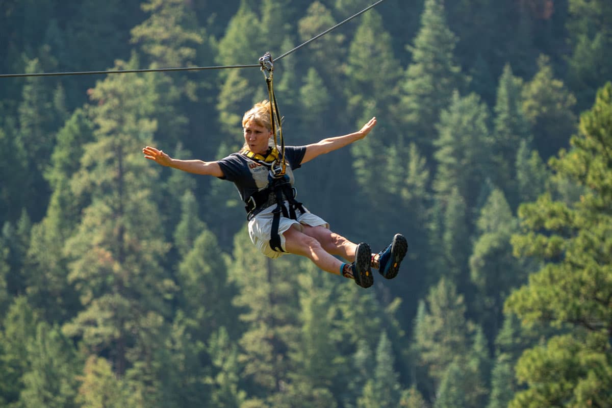 A person ziplining with arms spread out above the lush San Juan National Forest in Colorado.
