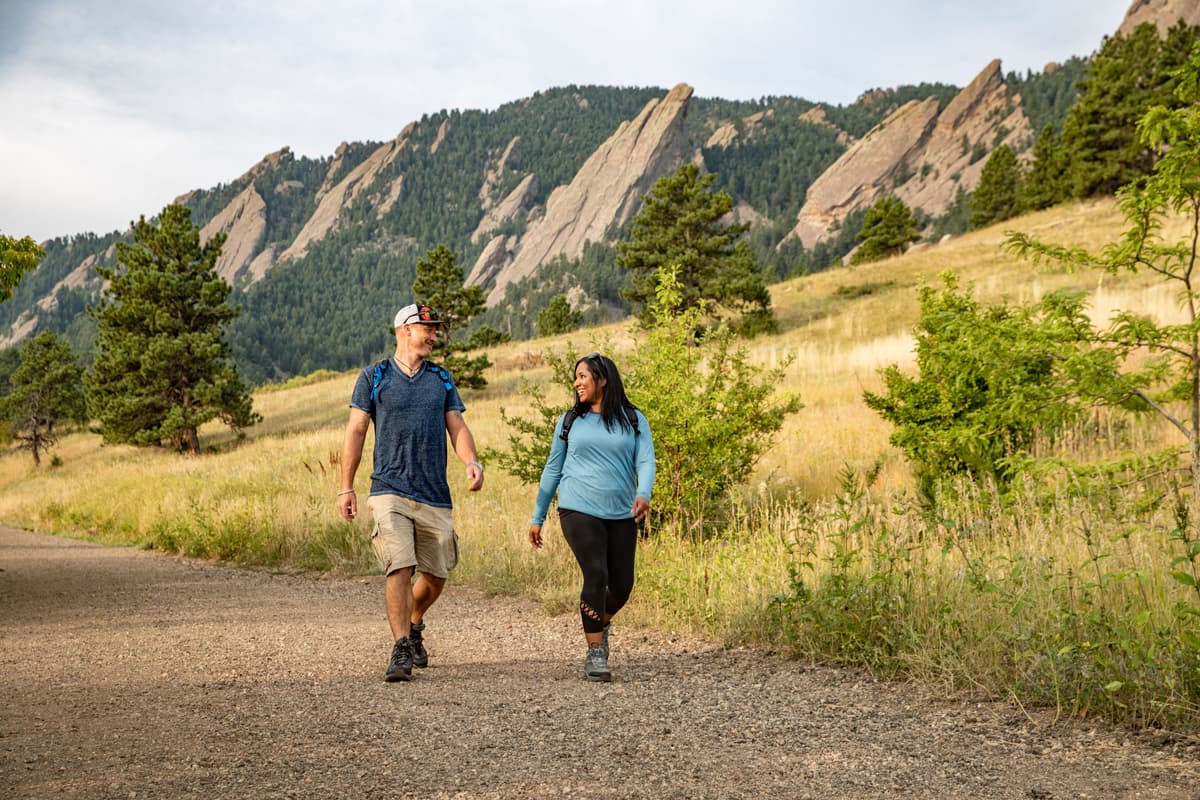 Two people walk along Chautauqua Trail with Boulder's iconic Flatirons in the background