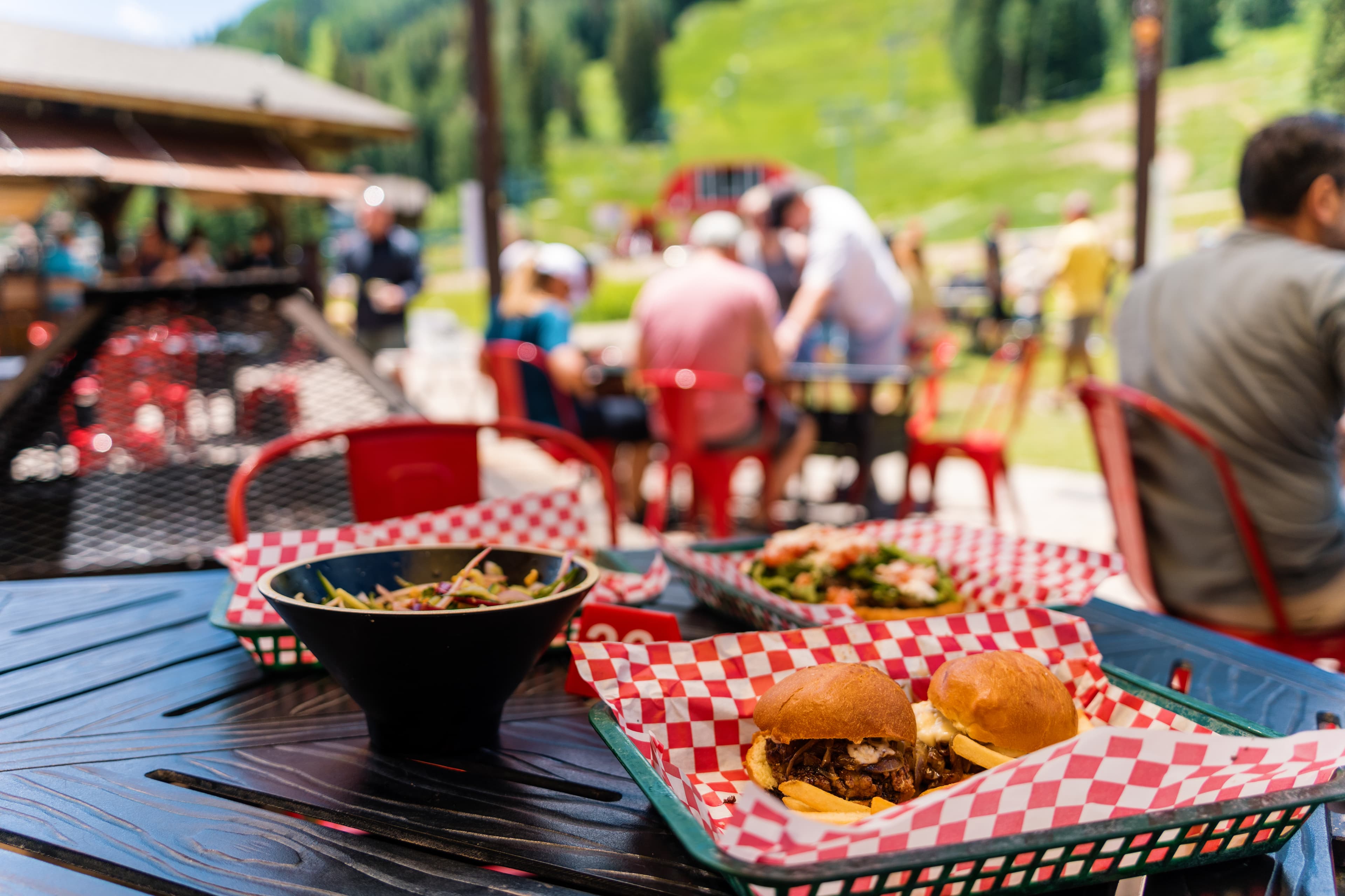 Meal trays with juicy hamburgers and crispy fries on an outdoor table with patio seating and a scenic backdrop.