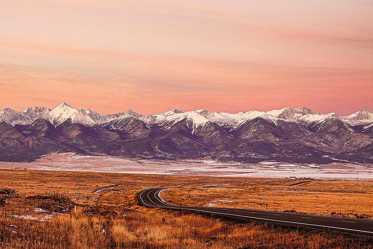 Sunset glow over a scenic road with snow-capped mountains in the background in Colorado.