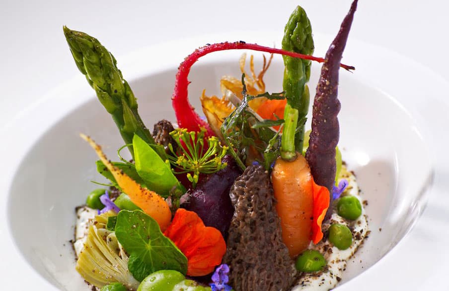 A white plate displays a sculptural view of various green, red and yellow veggies