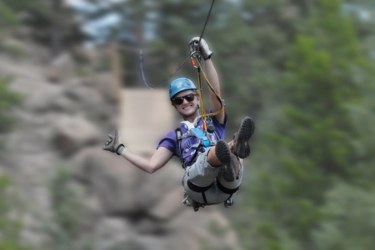 A person in a helmet smiles as they zipling across a rocky canyon in Idaho Springs