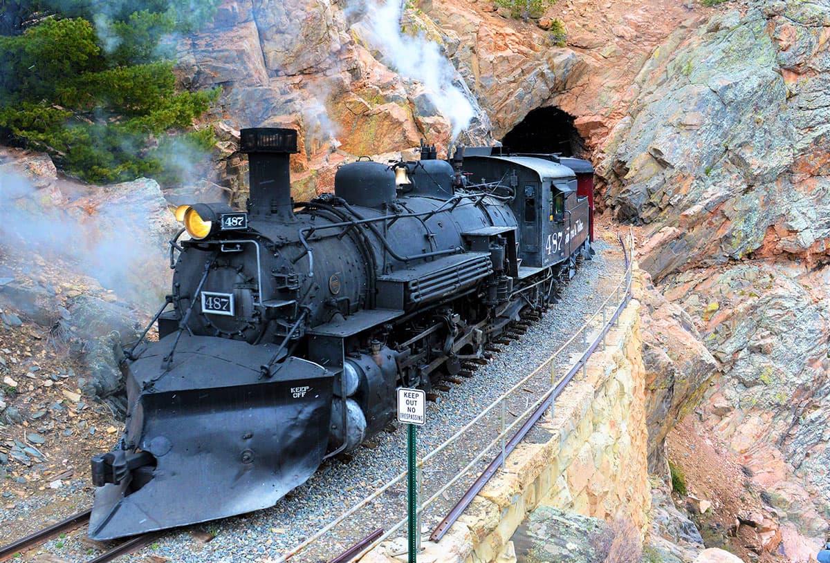 A black locomotive comes out of a rocky mountain cave