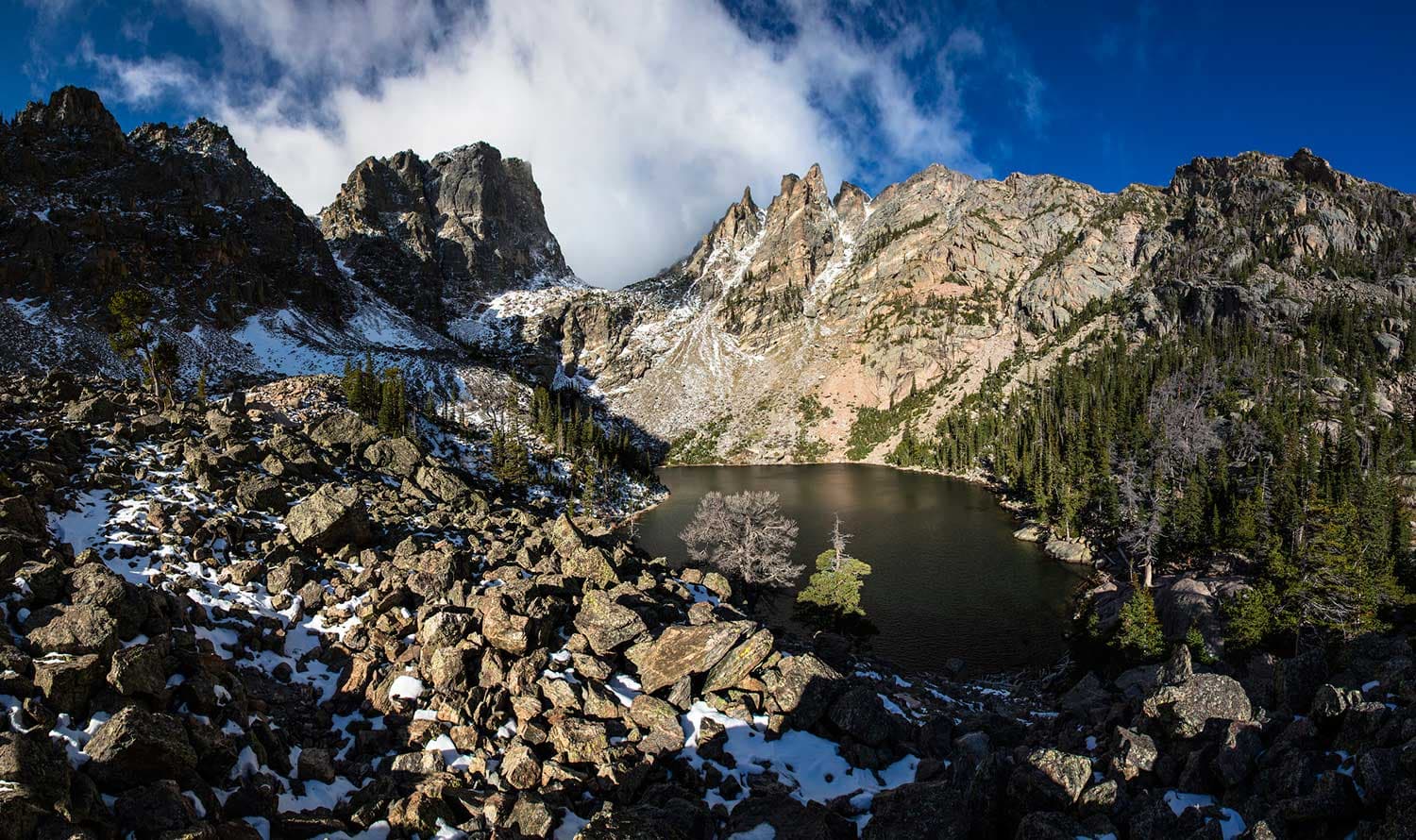 A small lake is surrounded by rocky and snowy mountains
