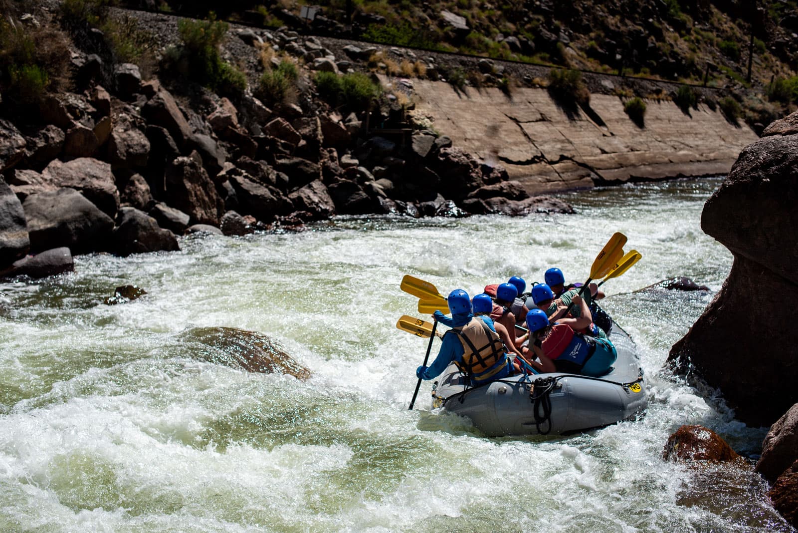 A raft of paddlers steers around a giant rock in the middle of the river