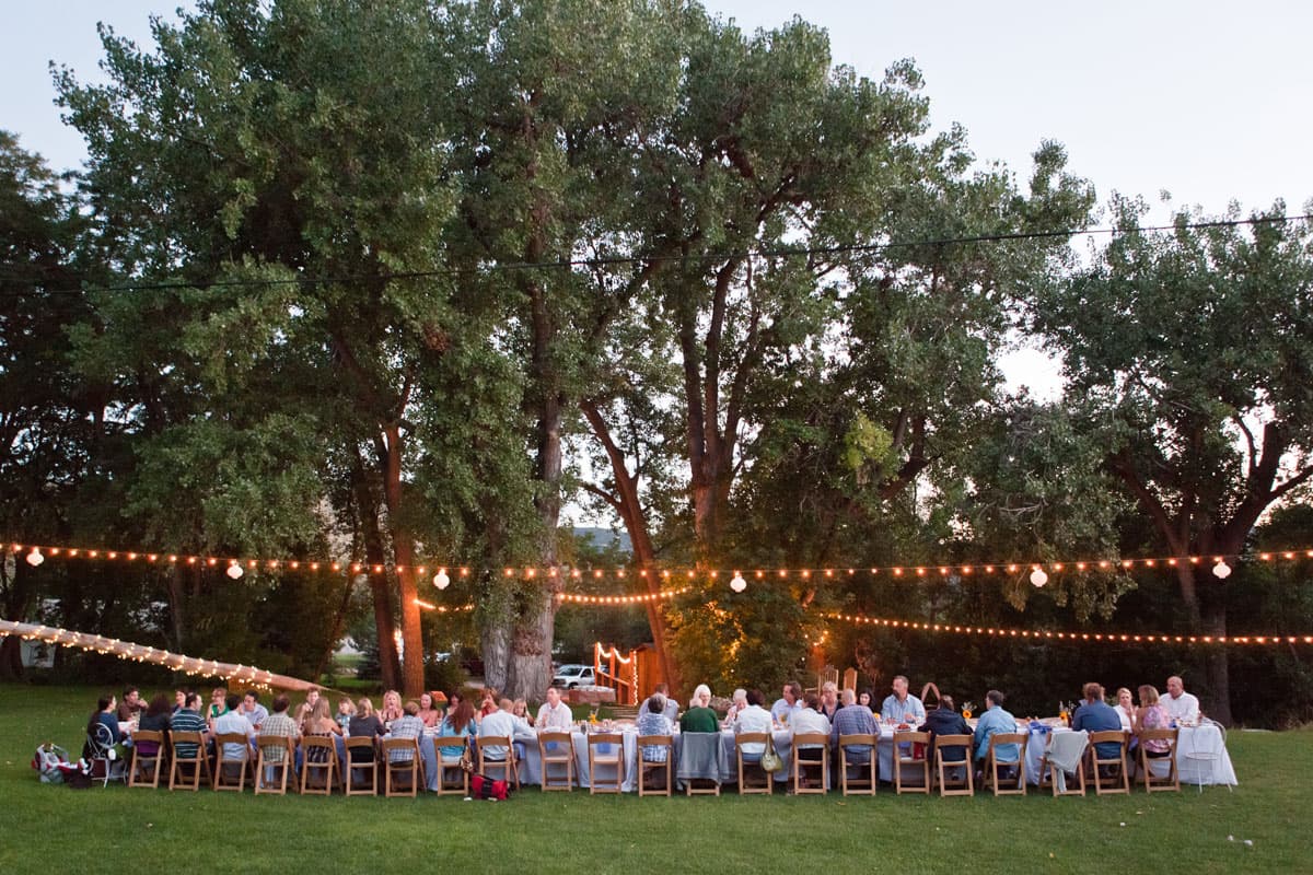 People sit at a long table below glowing lights at a farm dinner at Lyons Farmette