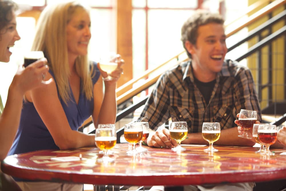 People laugh around a table, holding beers at the tasting room at New Belgium Brewing Co. in Fort Collins, CO