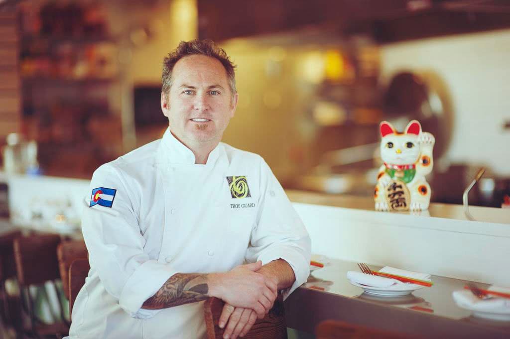 Star Colorado chef Troy Guard sits at the bar of his Colorado restaurant and poses next to a white neko cat.