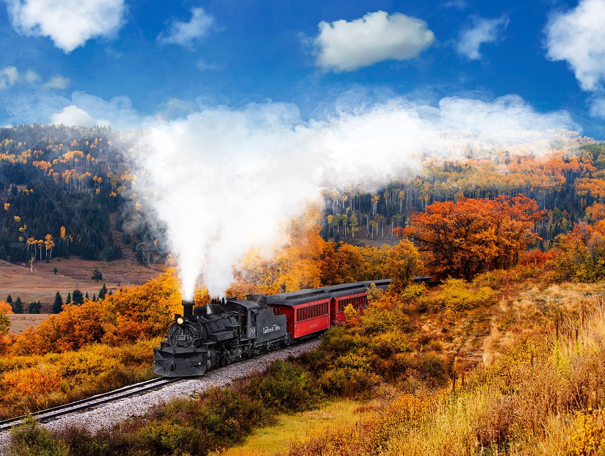 A train steams through a mountain pass full of colorful foliage