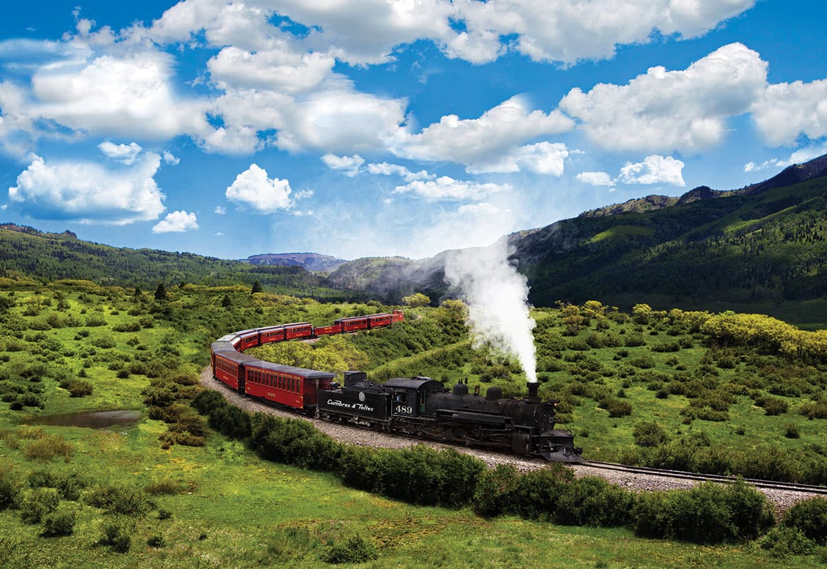 A train winds across tracks in a wide mountain landscape