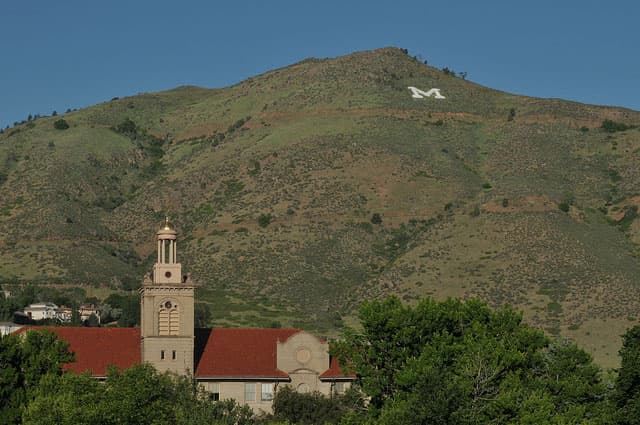 In Colorado, the tower of a campus building is seen against a grassy peak with the School of Mines "M" carved in the side.