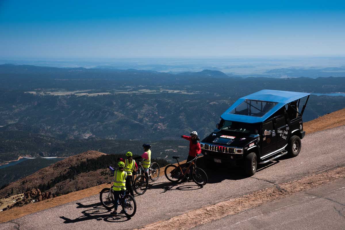 Four people on bikes pointing at beautiful views from Pikes Peak