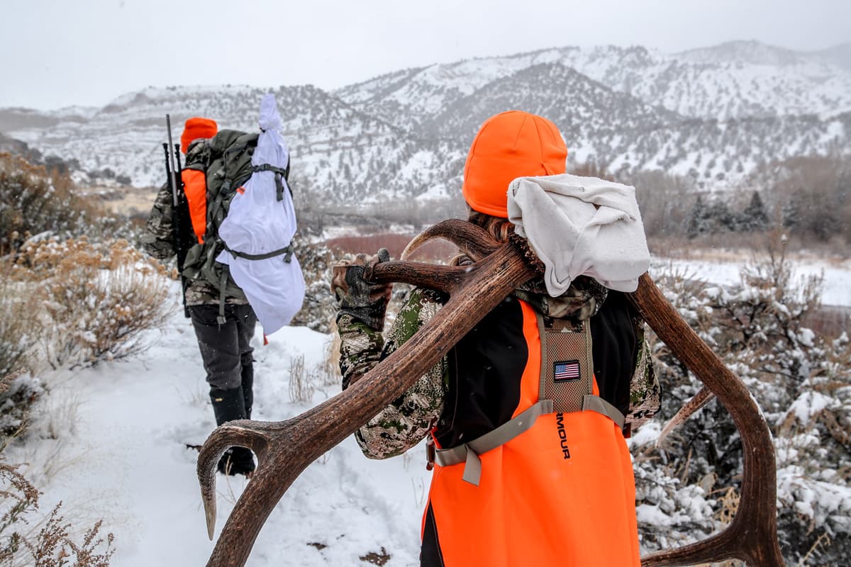 Hunters in camo and orange vesets and hats pack their bounty out of the woods