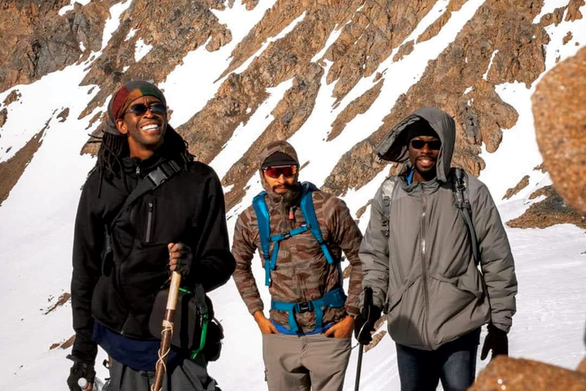 Three Black men in bundled in outdoor gear hike along a snowy trail