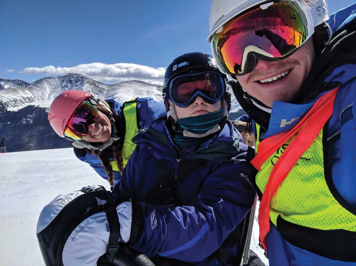 Three winter adventurers pose for a photo atop a mountain at the National Sports Center for the Disabled in Winter Park