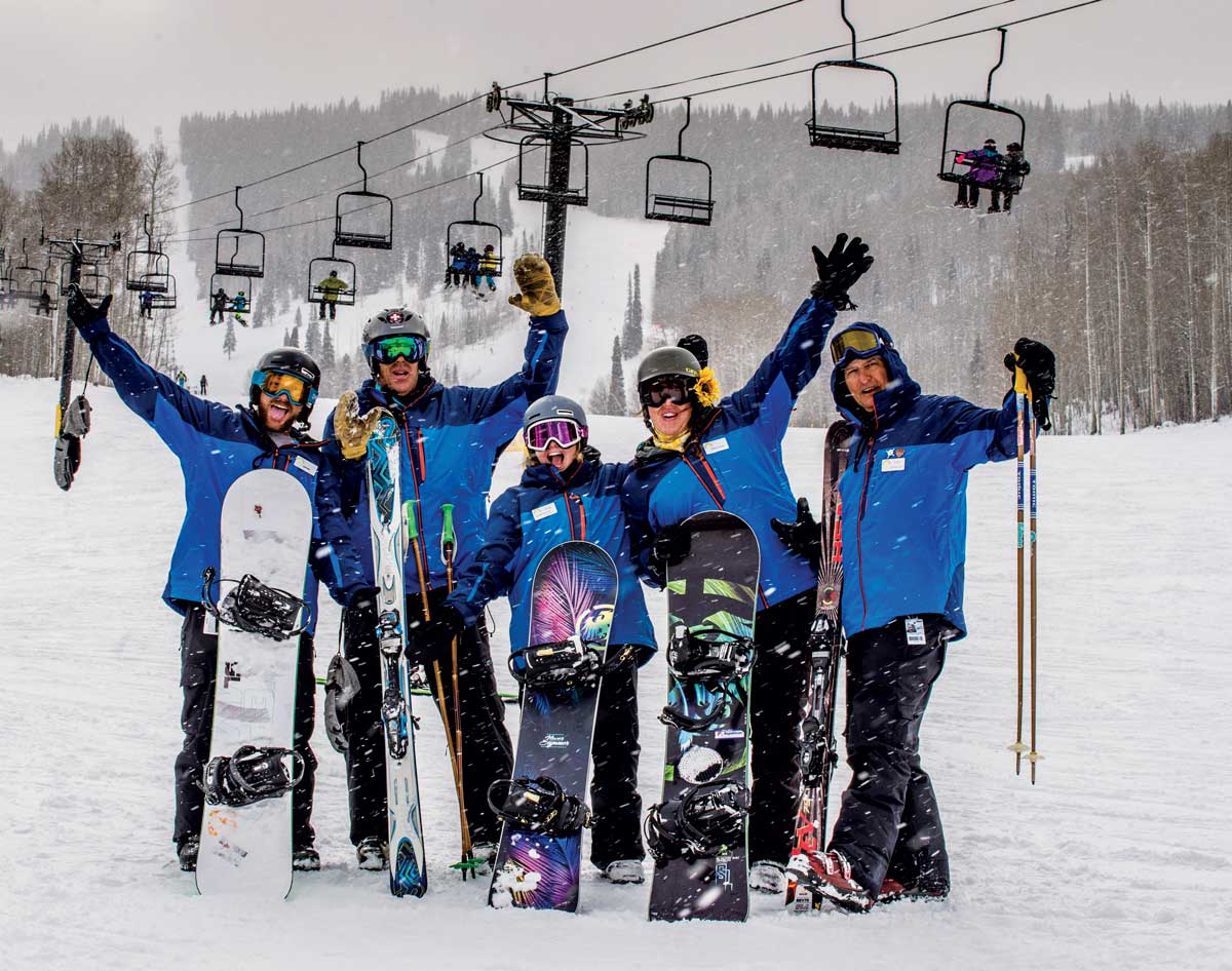 A group of skiers and boarders pose for a picture in matching two-tone blue jackets as snow falls at Sunlight Mountain Resort in Glenwood Springs