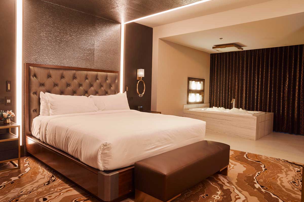 A beautifully made white-linen-covered bed on a chic marble-patterned rug with an in-room bathtub in the Terrace Suite at Monarch Casino Resort