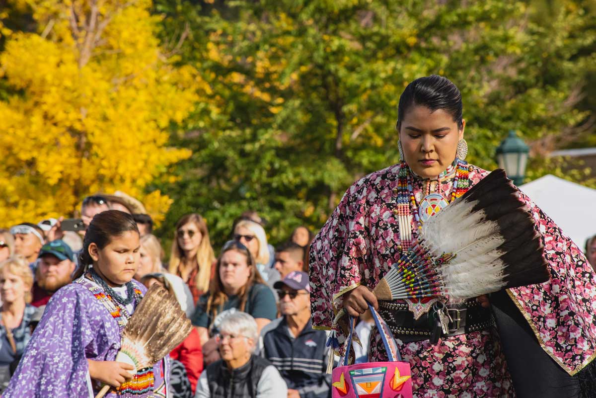 A Native American woman and girl perform a dance at Elk Fest in Estes Park while holding feathered fans while a crowd watches