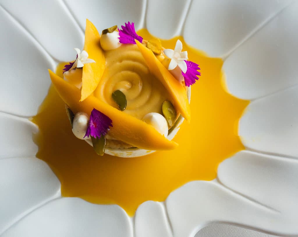 Bright orange mango sorbet topped with fresh mango and pink and white flowers at Frasca Food and Wine in Boulder, Colorado.