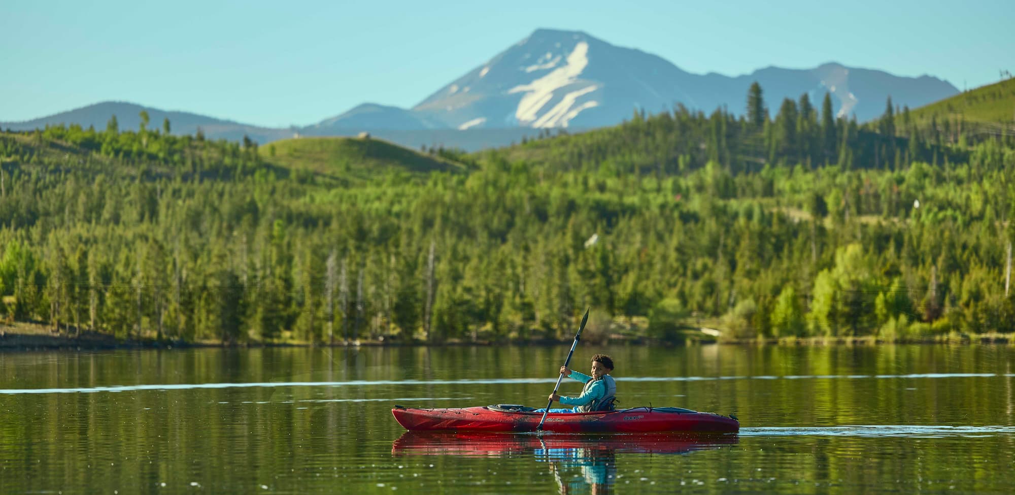 A person kayaks across a calm lake with mountains in the background in Frisco, Colorado