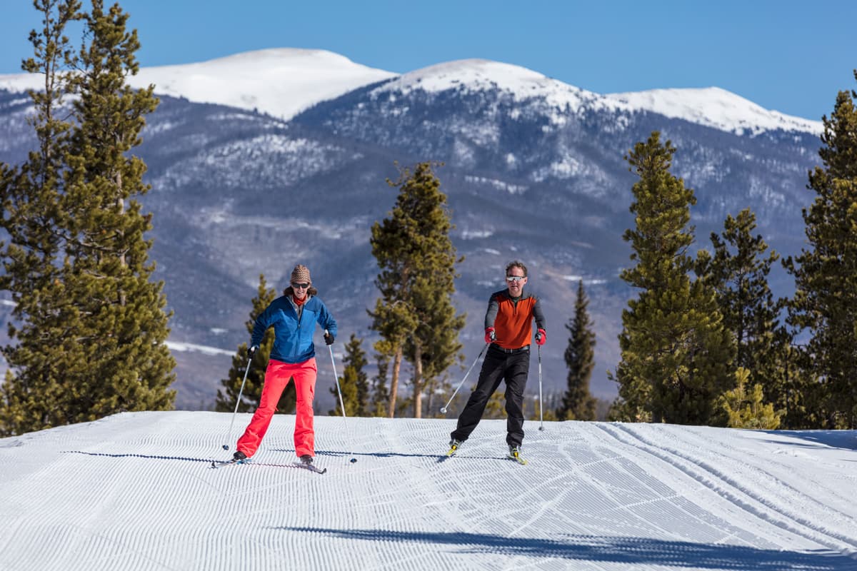 Two people cross-country skiing at Frisco Nordic Center with the mountains in the background in Frisco, Colorado