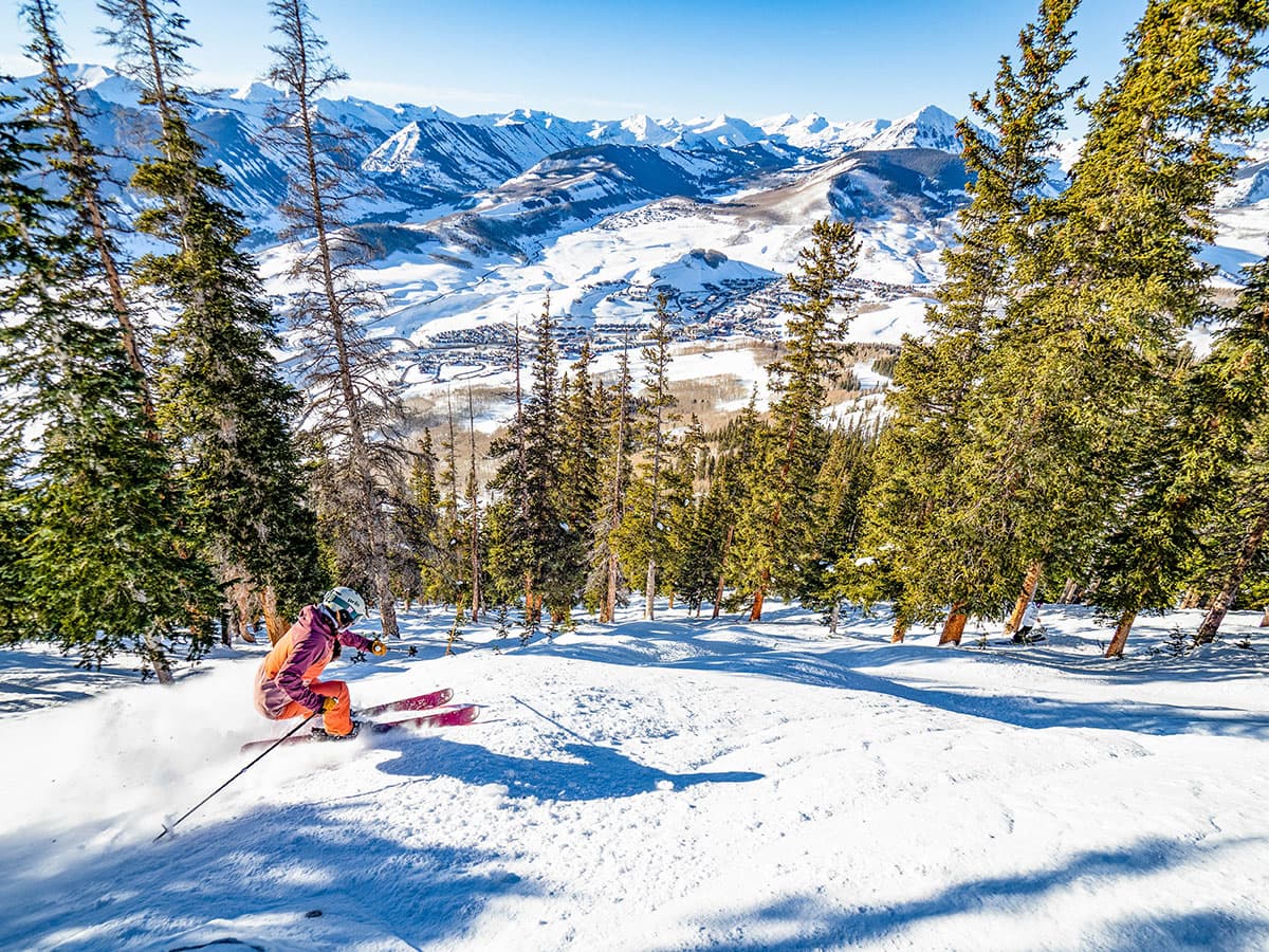 Aerial view of a skier going down a steep hill surrounded by snowy mountains and trees