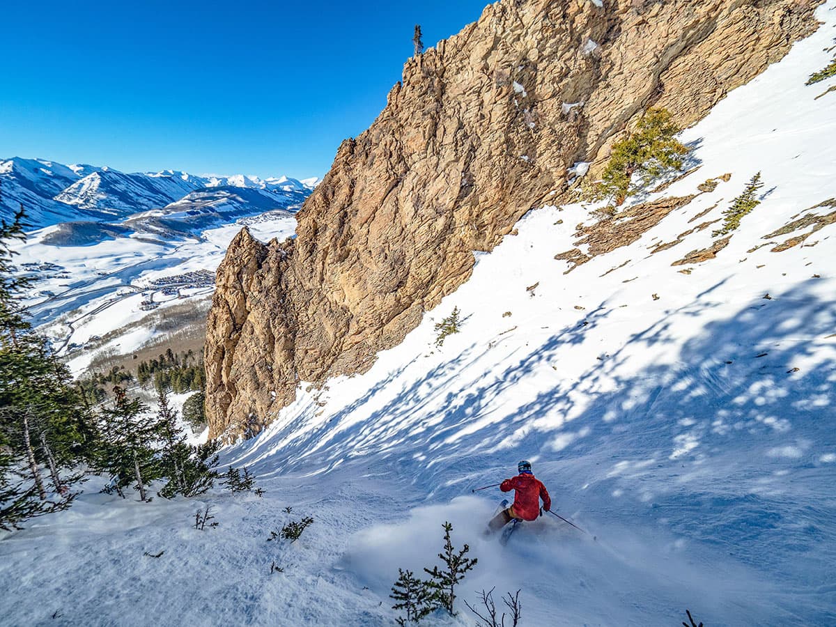 View of a skier on an extremely steep and narrow ski hill bordered by rock formations