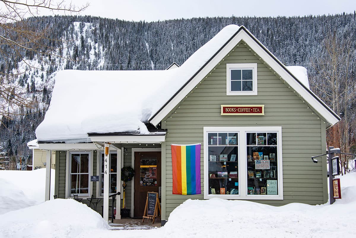 Green bungalow-style building with a snowy roof and snowy trees in the background