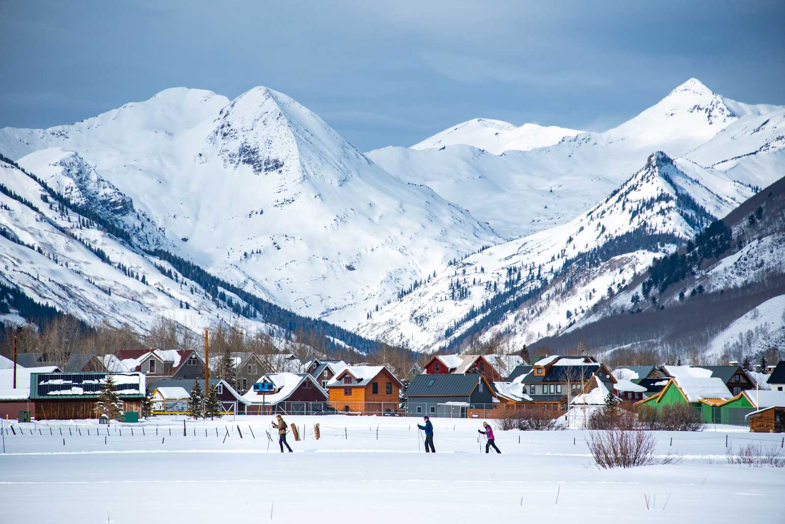 Three cross-country skiers cross a snowy meadow below snow-covered peaks in Crested Butte