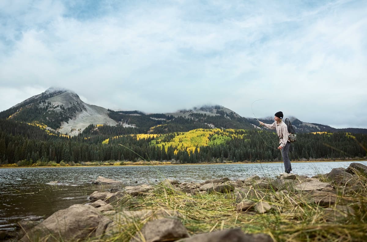 A person fly-fishes in a river with golden fall leaves in the background in Gunnison Valley, Colorado.